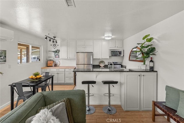 kitchen with an AC wall unit, kitchen peninsula, light hardwood / wood-style flooring, stainless steel appliances, and white cabinets