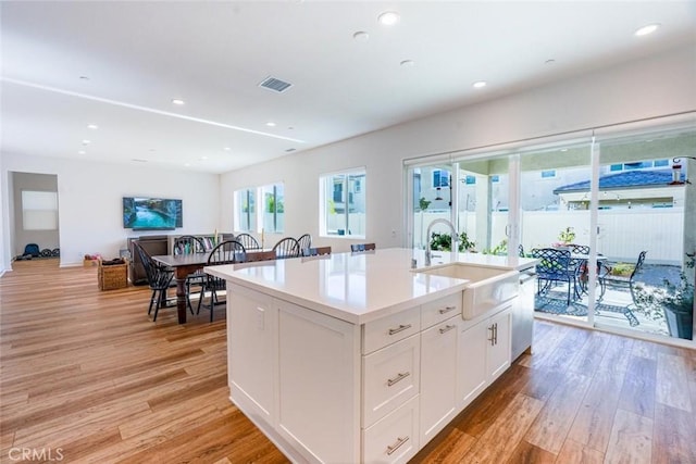 kitchen featuring white cabinets, an island with sink, a sink, and light wood-style floors