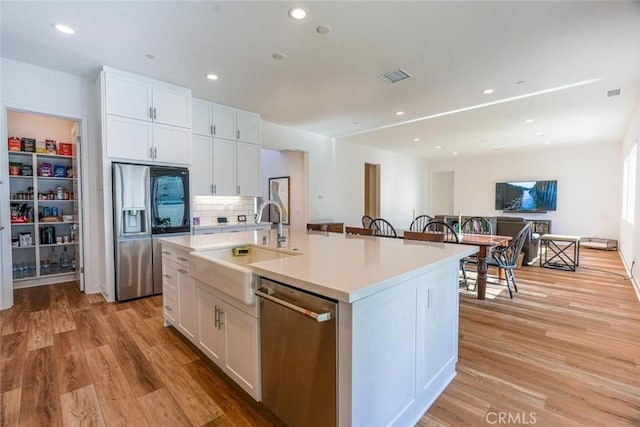 kitchen with white cabinets, stainless steel appliances, a kitchen island with sink, and sink