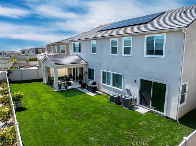 back of house with a fenced backyard, roof mounted solar panels, central AC, and a yard