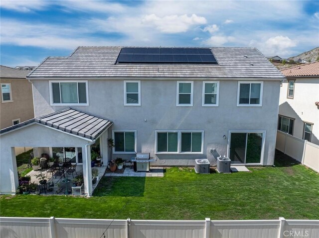 rear view of property featuring a yard, solar panels, a fenced backyard, and stucco siding