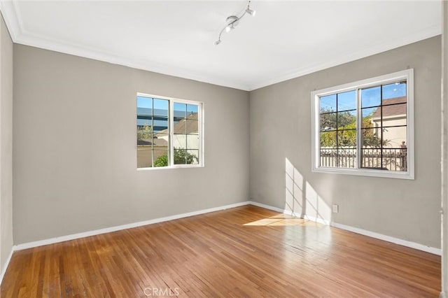 unfurnished room featuring a healthy amount of sunlight, crown molding, baseboards, and wood finished floors