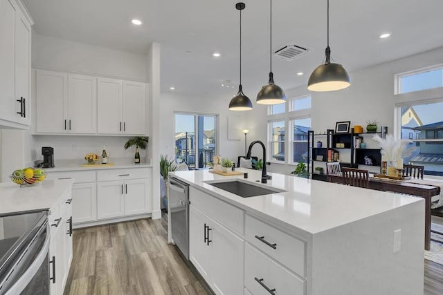 kitchen with sink, pendant lighting, white cabinets, and an island with sink