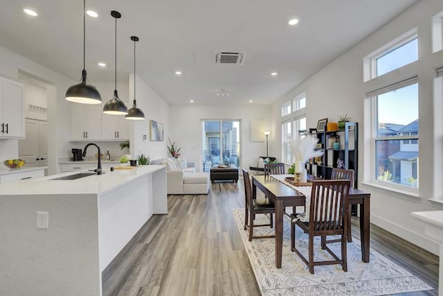 kitchen with a wealth of natural light, white cabinetry, sink, hanging light fixtures, and light wood-type flooring