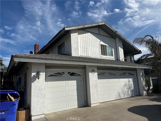 view of side of home with a chimney, roof with shingles, concrete driveway, an attached garage, and stucco siding