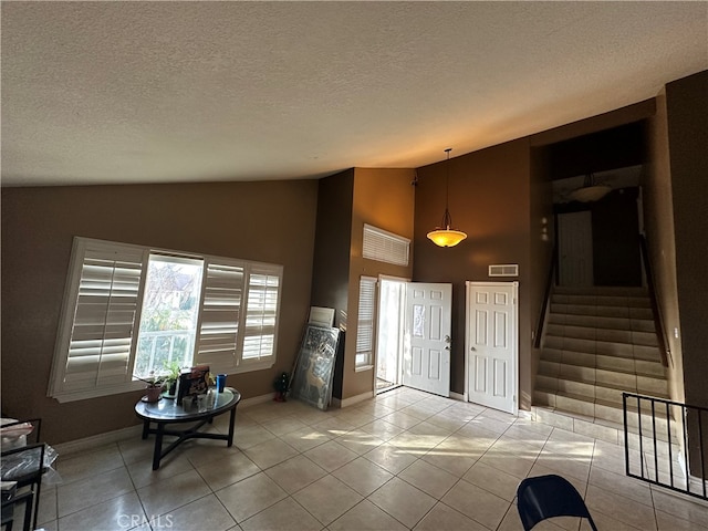 foyer with a textured ceiling, baseboards, light tile patterned floors, and stairway