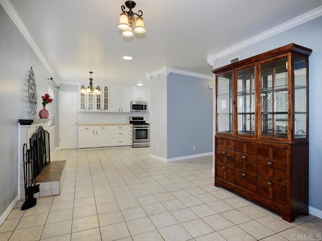 kitchen featuring stainless steel appliances, a notable chandelier, ornamental molding, white cabinets, and backsplash