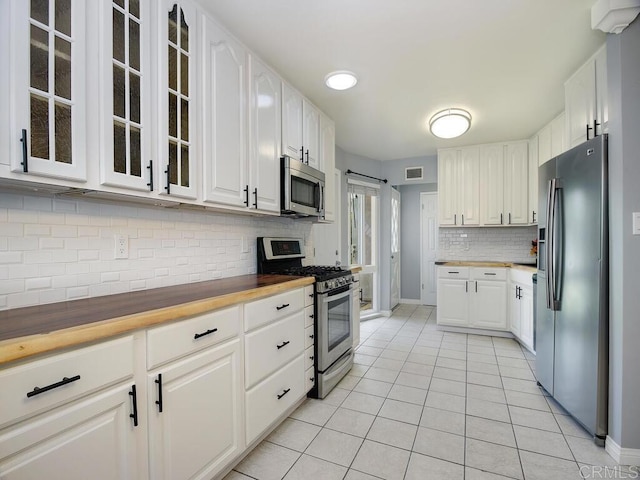 kitchen with stainless steel appliances, butcher block countertops, light tile patterned floors, and white cabinetry