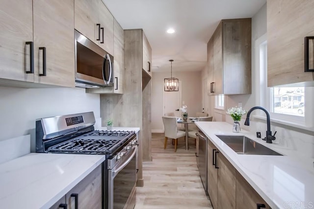 kitchen featuring sink, decorative light fixtures, light hardwood / wood-style flooring, appliances with stainless steel finishes, and light stone countertops