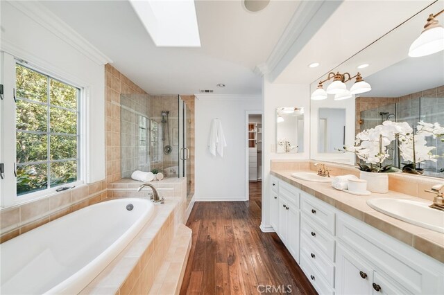 bathroom featuring wood-type flooring, a skylight, ornamental molding, vanity, and plus walk in shower