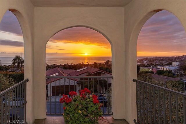 balcony at dusk featuring a water view