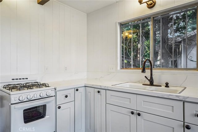 kitchen featuring sink, light stone counters, wooden walls, and white range with gas stovetop