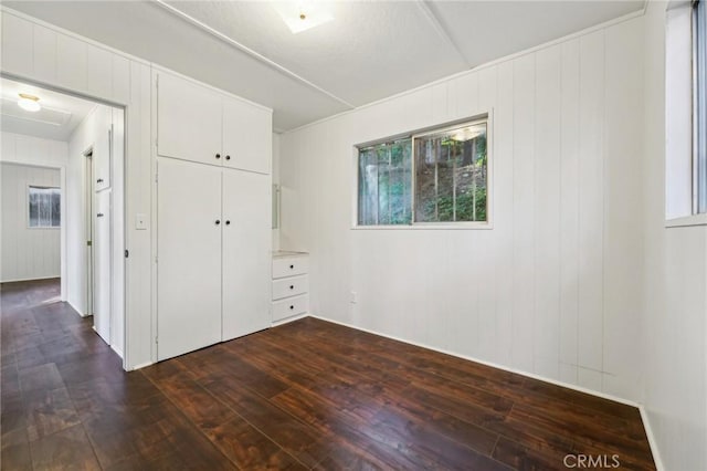 unfurnished bedroom featuring a closet, wood walls, and dark hardwood / wood-style floors