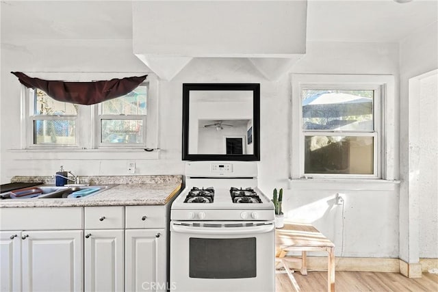 kitchen featuring sink, white cabinets, white gas range oven, and light hardwood / wood-style floors