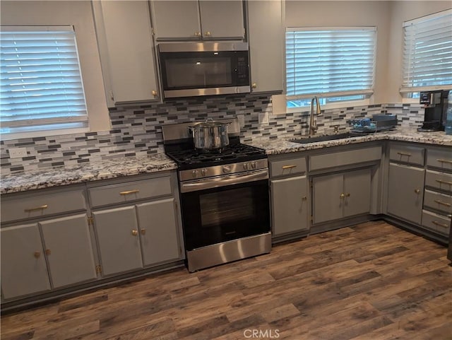 kitchen featuring gray cabinets, stainless steel appliances, decorative backsplash, light stone counters, and sink