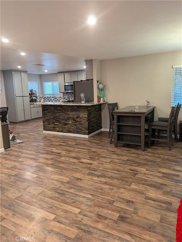 kitchen with appliances with stainless steel finishes, decorative backsplash, dark hardwood / wood-style flooring, and kitchen peninsula