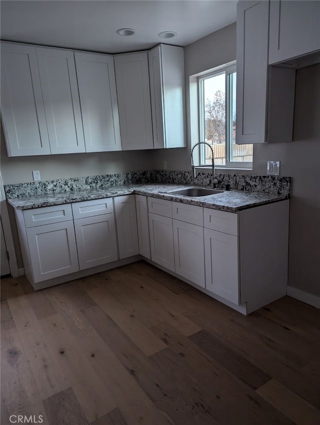 kitchen with white cabinetry, light hardwood / wood-style flooring, light stone counters, and sink