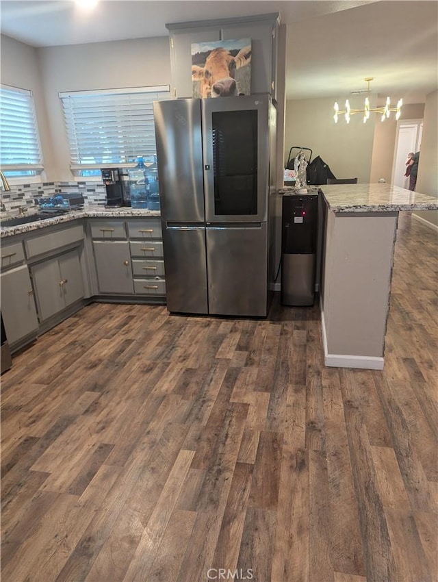 kitchen featuring light stone countertops, dark hardwood / wood-style flooring, tasteful backsplash, stainless steel fridge, and kitchen peninsula