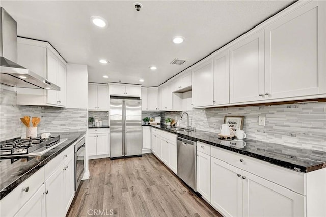 kitchen featuring white cabinets, wall chimney exhaust hood, stainless steel appliances, sink, and light hardwood / wood-style flooring