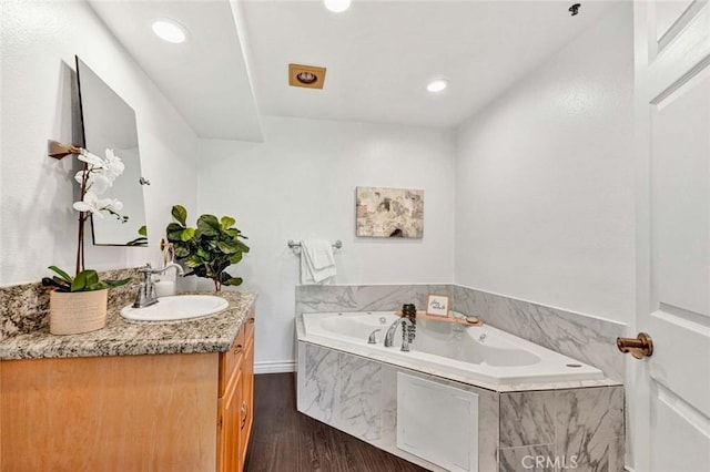 bathroom with wood-type flooring, tiled tub, and vanity