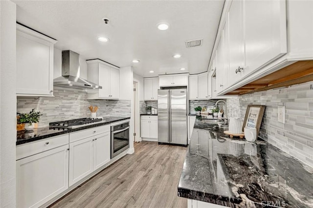 kitchen featuring stainless steel appliances, wall chimney exhaust hood, white cabinets, and dark stone counters