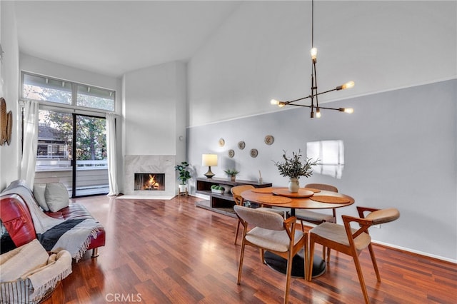 dining space with hardwood / wood-style flooring, a high end fireplace, a chandelier, and a high ceiling