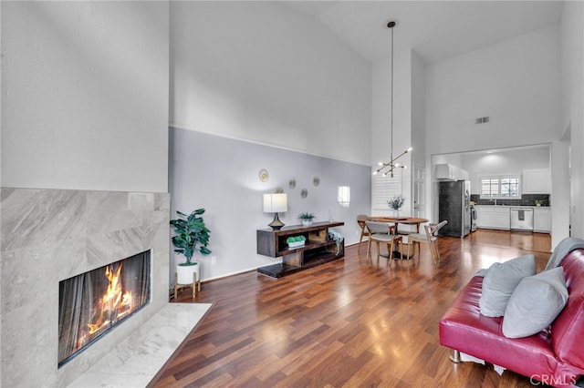 living room featuring an inviting chandelier, a high end fireplace, high vaulted ceiling, and wood-type flooring