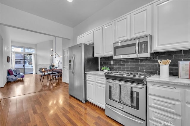 kitchen with light hardwood / wood-style flooring, stainless steel appliances, light stone countertops, decorative backsplash, and white cabinets