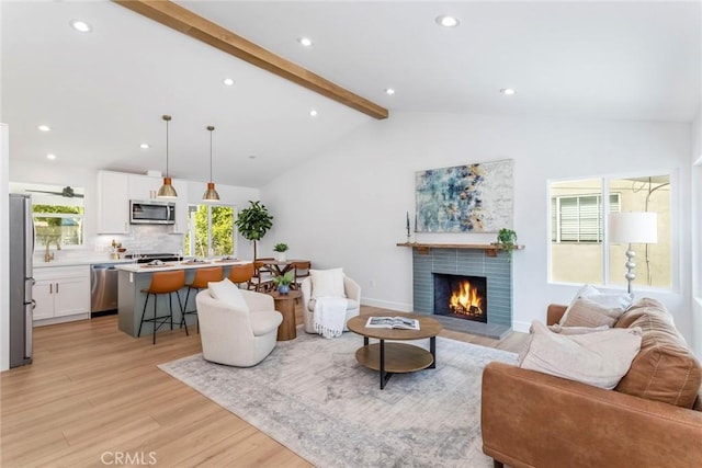 living room with vaulted ceiling with beams, a warm lit fireplace, recessed lighting, baseboards, and light wood finished floors