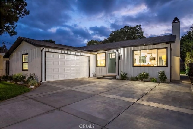 view of front of property with a garage, board and batten siding, a chimney, and concrete driveway