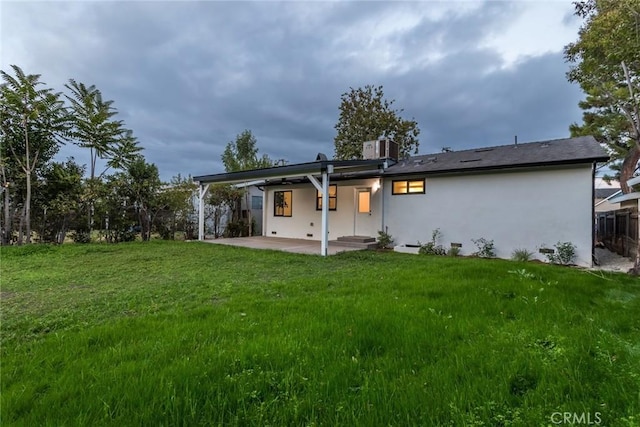 rear view of property featuring a patio, stucco siding, a lawn, central AC, and fence