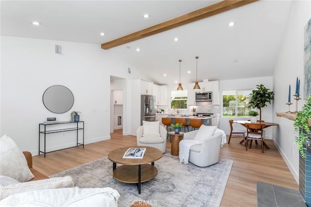 living room featuring light wood finished floors, baseboards, visible vents, beamed ceiling, and high vaulted ceiling