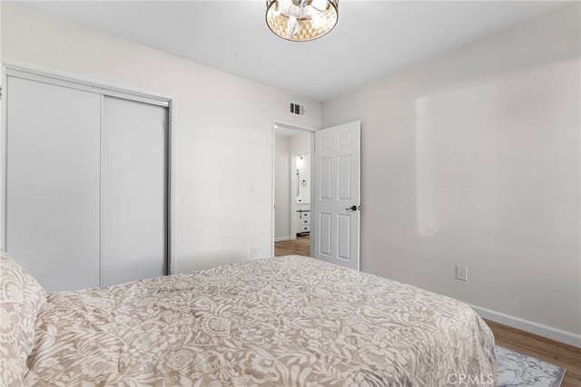 bedroom with baseboards, a closet, wood finished floors, and visible vents