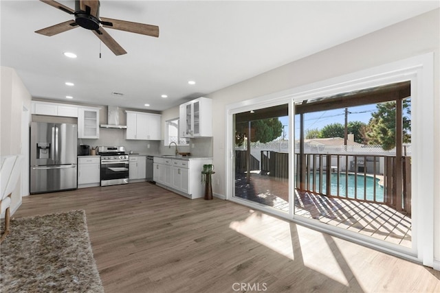kitchen with wall chimney range hood, stainless steel appliances, a sink, and wood finished floors