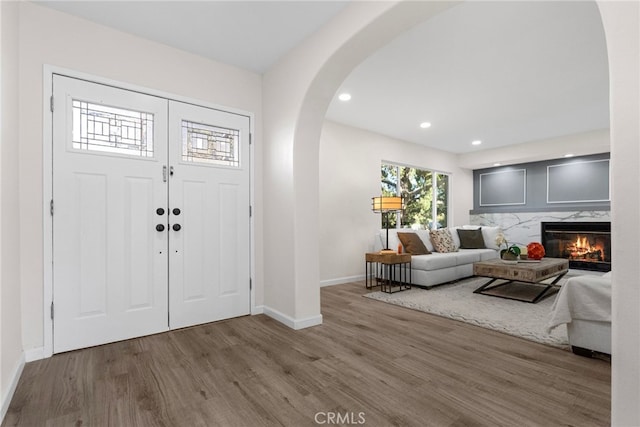 entryway featuring wood finished floors, a fireplace, baseboards, recessed lighting, and arched walkways