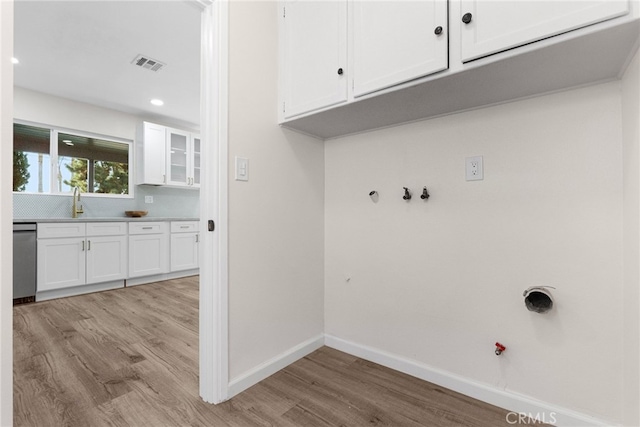 laundry room with visible vents, hookup for a gas dryer, cabinet space, baseboards, and light wood finished floors
