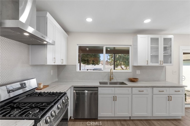 kitchen featuring appliances with stainless steel finishes, a sink, wall chimney exhaust hood, white cabinetry, and backsplash