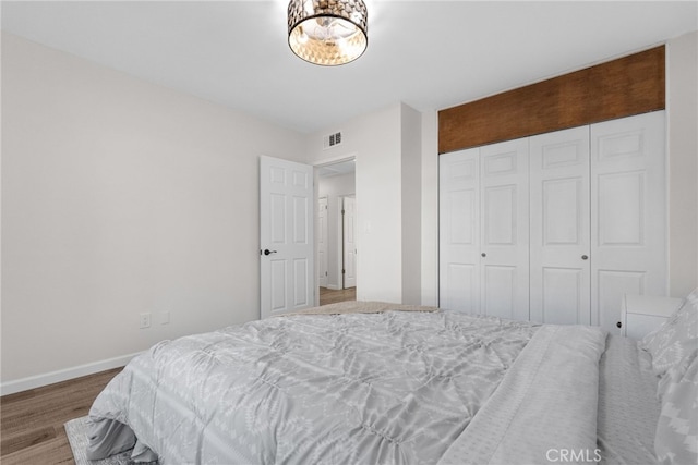 bedroom with baseboards, visible vents, wood finished floors, and a closet
