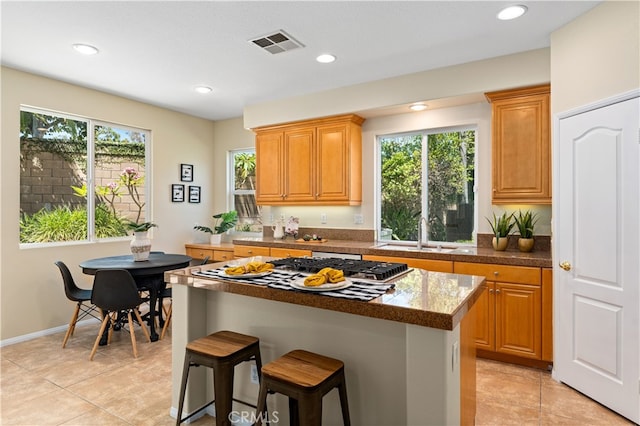 kitchen featuring a center island, dark stone counters, sink, light tile patterned flooring, and a breakfast bar