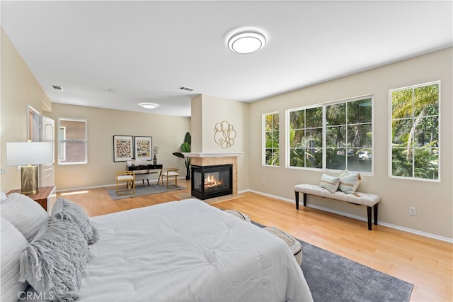 bedroom with multiple windows, a tiled fireplace, and light wood-type flooring