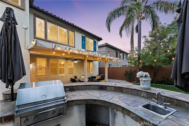 patio terrace at dusk featuring sink, an outdoor kitchen, and grilling area