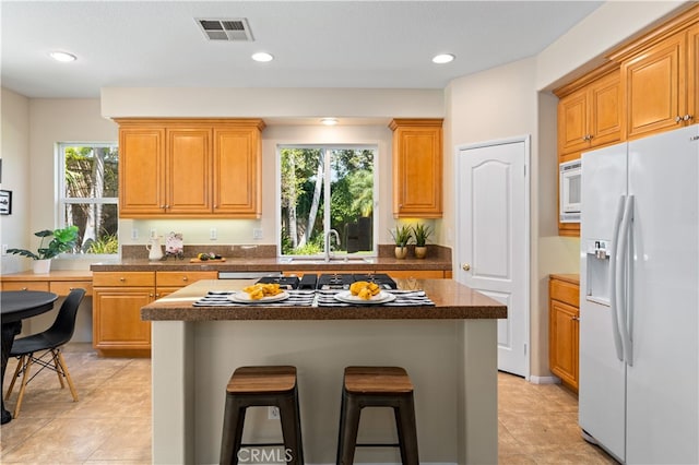 kitchen with a breakfast bar, white appliances, a center island, and sink