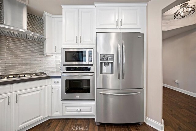 kitchen with white cabinets, wall chimney exhaust hood, dark hardwood / wood-style flooring, stainless steel appliances, and decorative backsplash