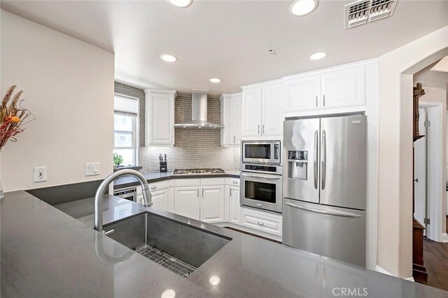 kitchen with white cabinetry, appliances with stainless steel finishes, backsplash, wall chimney range hood, and sink