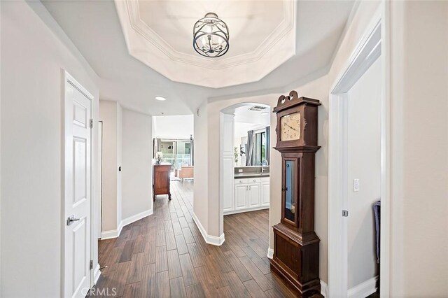 hall featuring dark hardwood / wood-style flooring, sink, ornamental molding, a notable chandelier, and a tray ceiling