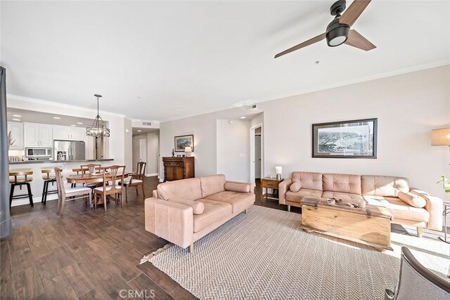 living room with crown molding, dark wood-type flooring, and ceiling fan with notable chandelier