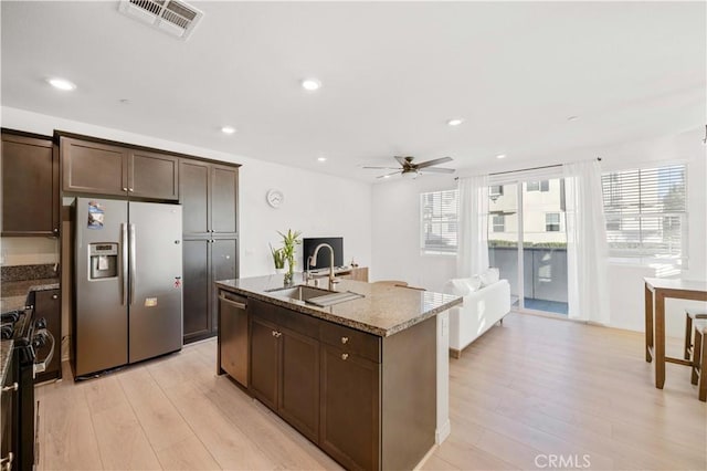 kitchen featuring light stone countertops, stainless steel appliances, sink, a center island with sink, and dark brown cabinets