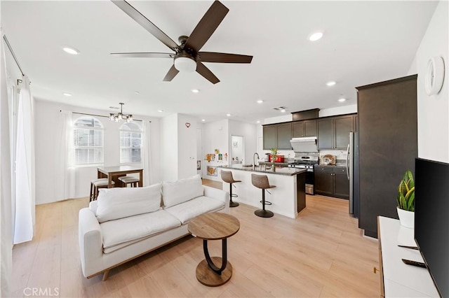 living room with ceiling fan with notable chandelier, sink, and light wood-type flooring