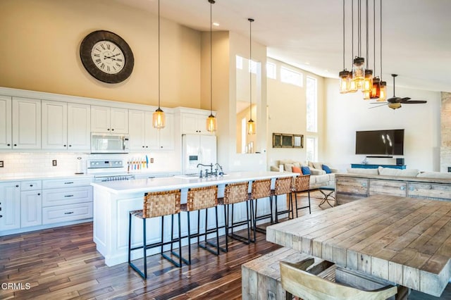 kitchen featuring ceiling fan, white appliances, hanging light fixtures, white cabinets, and a breakfast bar