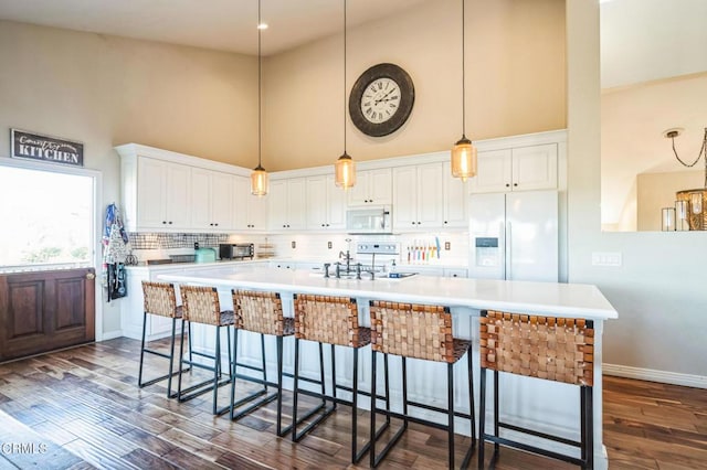 kitchen with white cabinetry, a large island, a high ceiling, white appliances, and pendant lighting